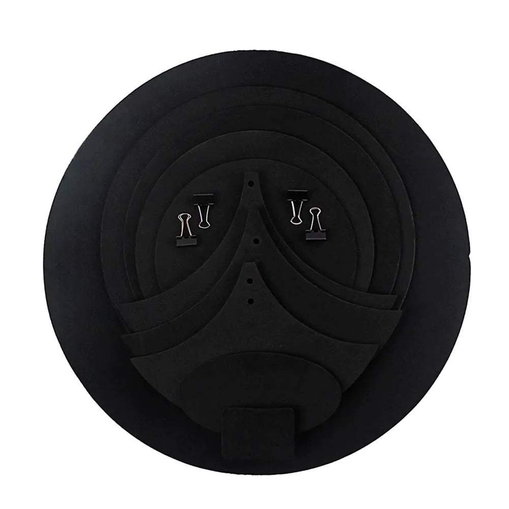 Black circular foam drum mute pad with concentric rings and two silver paper clips on top for drumming practice