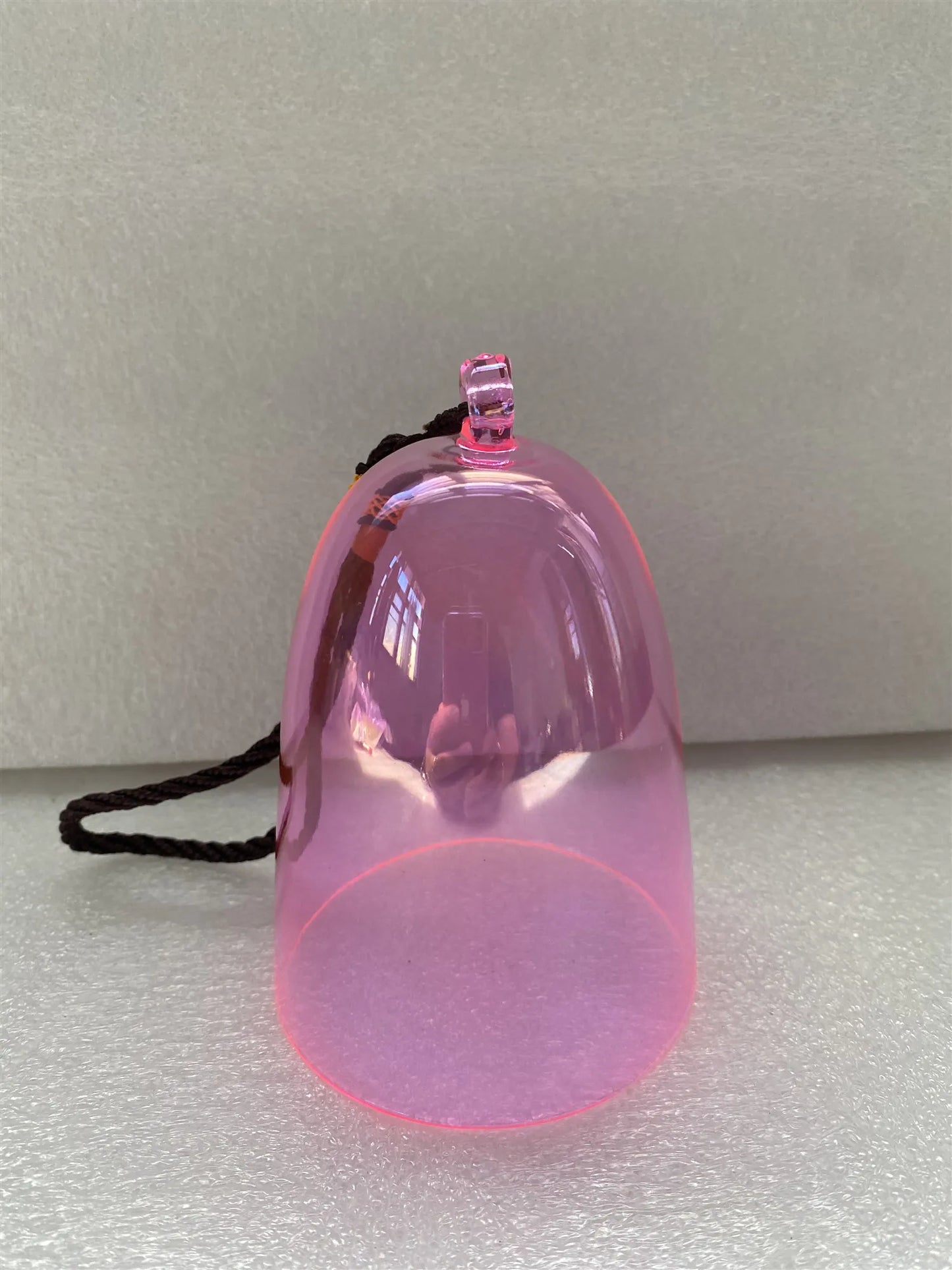 A translucent pink crystal singing bell pendant in the shape of a musical note with a black cord attached