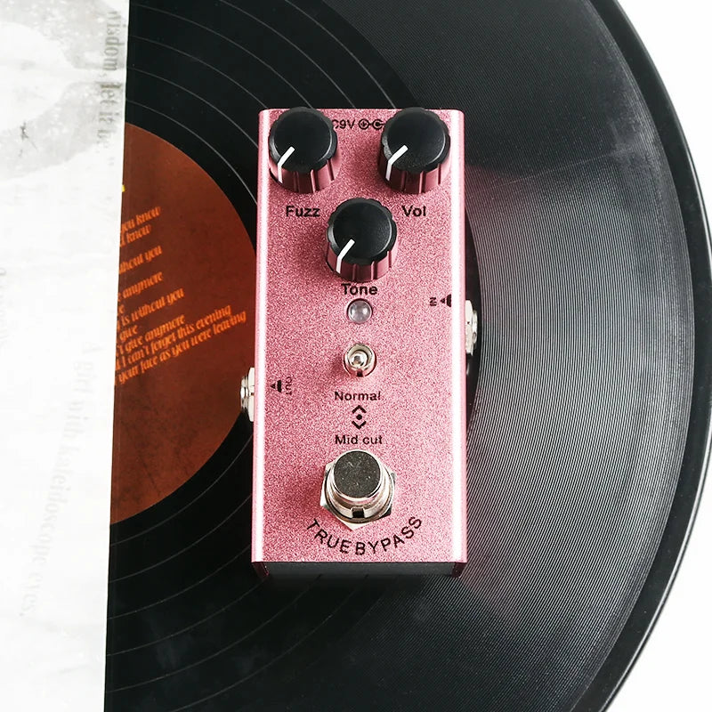A pink glittery metal electric guitar effect pedal with control knobs overdrive fuzz tone and vol for distortion tremolo delay