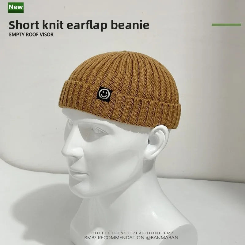 A tan short ribbed knit hip hop beanie with earflaps and a black patch smiley face for men and women winter use