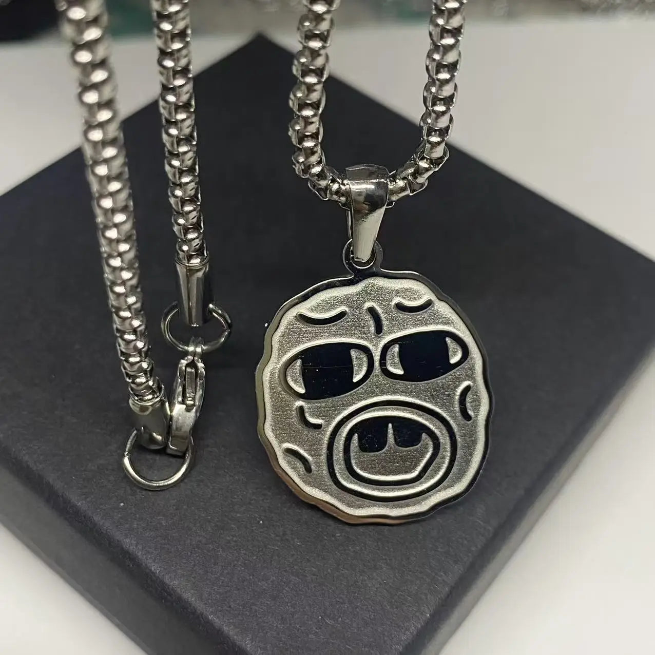 Silver-toned stainless steel hip hop necklace with circular textured face and black inlaid eyes, ideal rapper fan gift