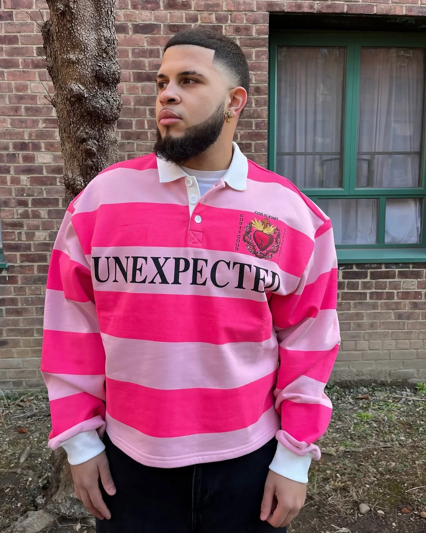 A vibrant pink striped rugby-style long sleeved polo shirt y2k with bold black unexpected lettering and crest patch american harajuku fashion