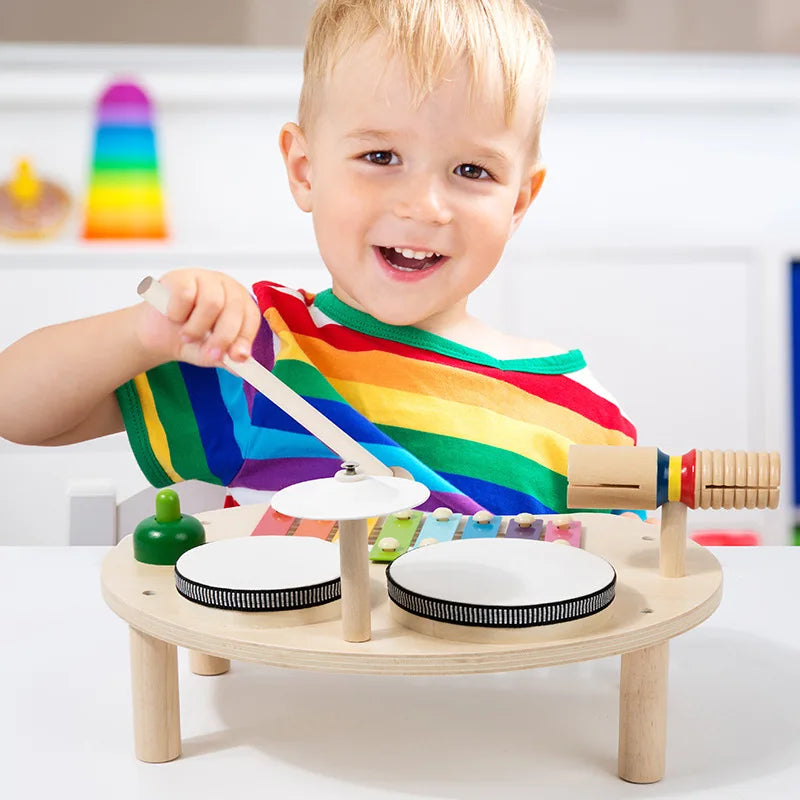 Wooden baby music table featuring white drums with black rims, colorful mallets, and a rainbow xylophone for montessori early educational play