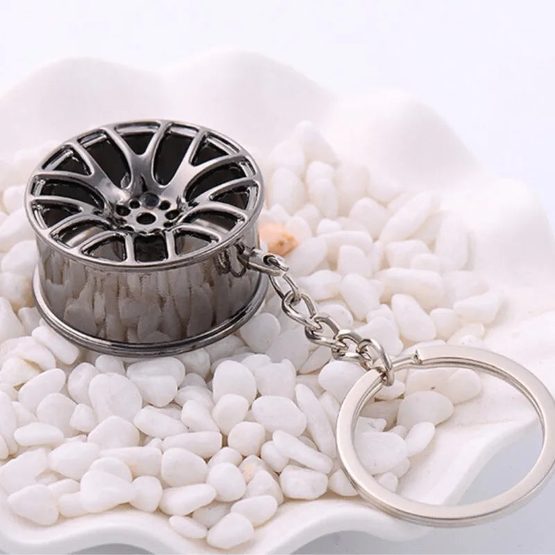 Silver metallic miniature car wheel rim keychain with intricate spokes and attached chain as hub key chain or car key ring