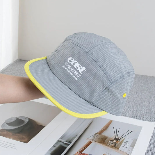 Gray and yellow five-panel baseball cap with subtle grid pattern and white embroidered branding, breathable and quick-drying
