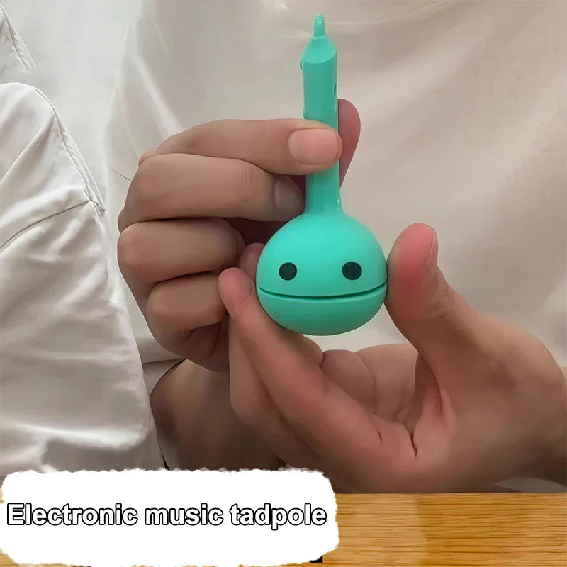 A teal cartoonish electronic music tadpole otamatone mini electronic toy with simple black dot eyes and musical notes design