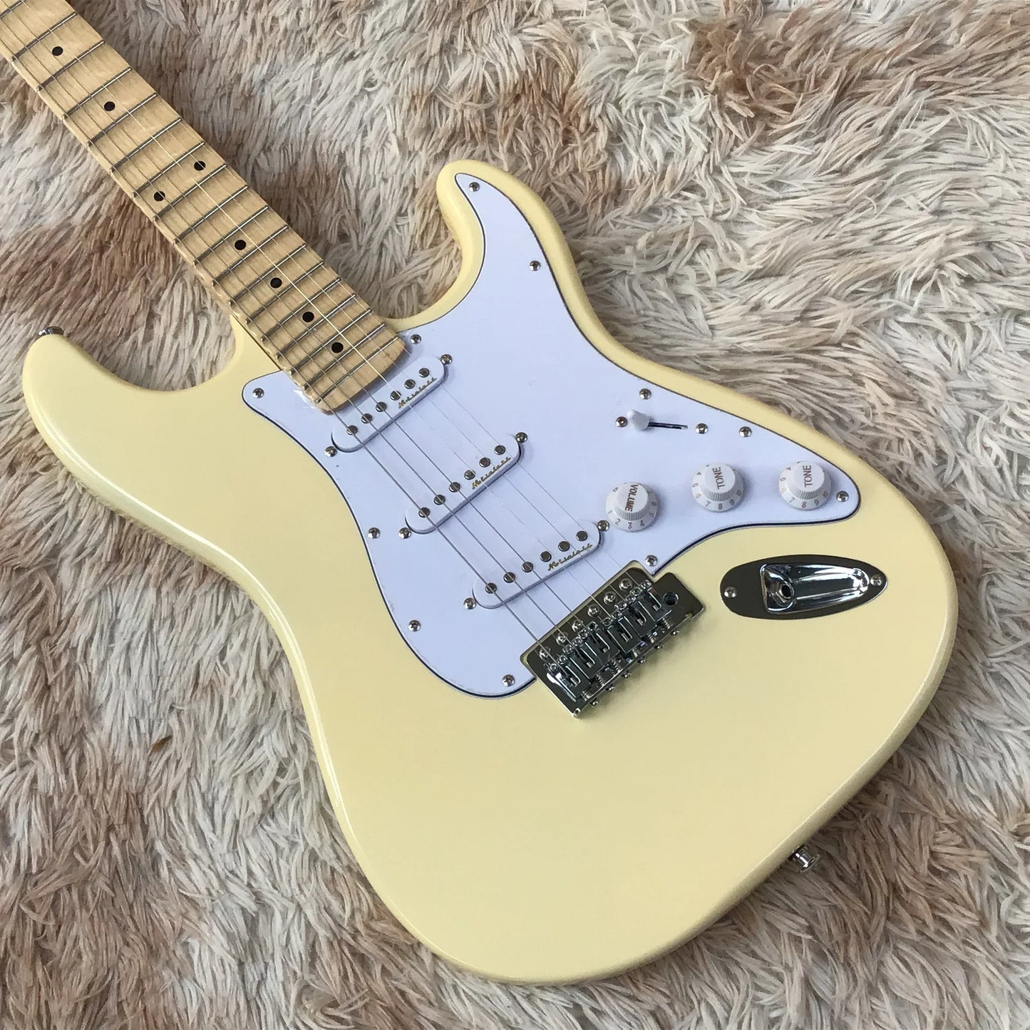 Cream-colored electric guitar with maple fingerboard features white pickguard and sparkling sss chrome hardware