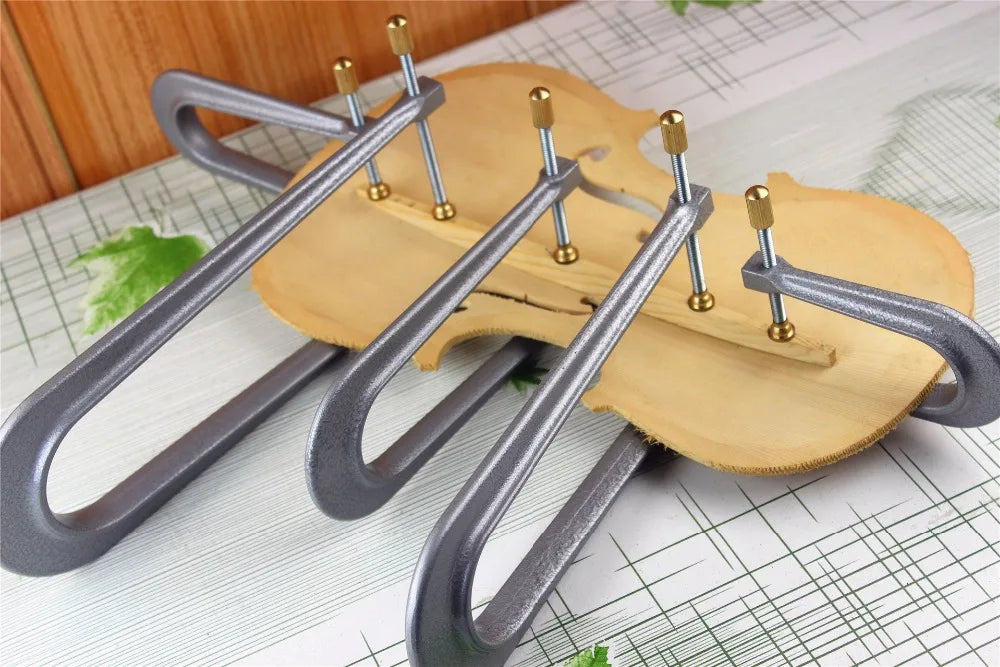 Three metallic violin bass-bar clamps with brass adjustment knobs on wood for viola violin making tools
