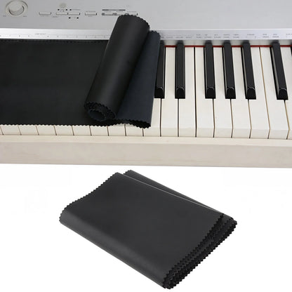 Black microfiber piano key cleaning cloth neatly folded beside a piano keyboard dust cover for keys upright pianos