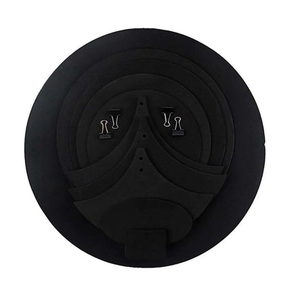 Black circular foam drum mute pad with concentric rings and two silver paper clips on top for drumming practice