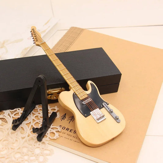 A light-colored wooden mini electric guitar with black pickguard and silver hardware displayed on support miniature model stand