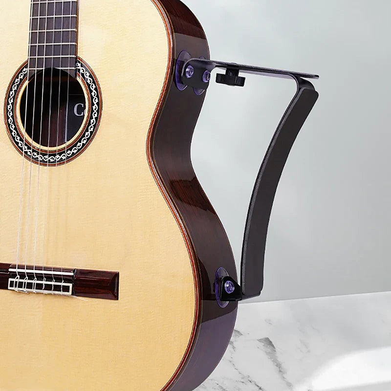 Black metal acoustic guitar footrest arm attached to classical guitar with light wood body and dark brown binding