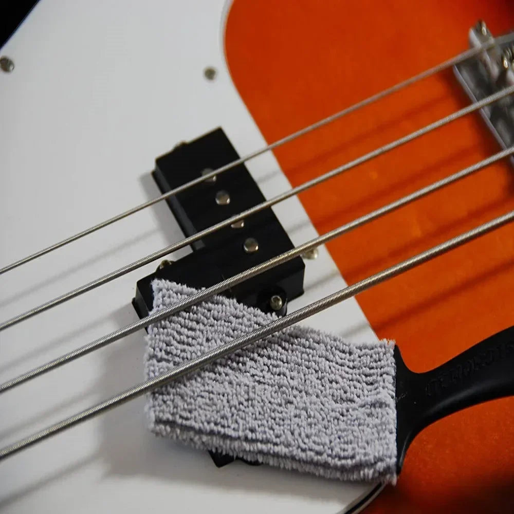 Gray microfiber cloth resting on black bridge of orange white electric bass guitar for string fingerboard cleaning dust removal brush
