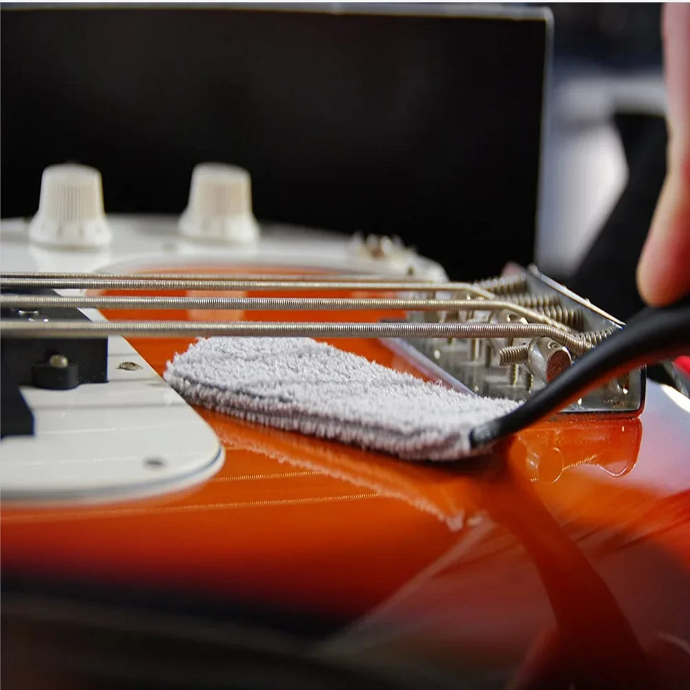A white microfiber cloth on the glossy orange body of an electric guitar with guitar care brush for dust removal and string fingerboard cleaning