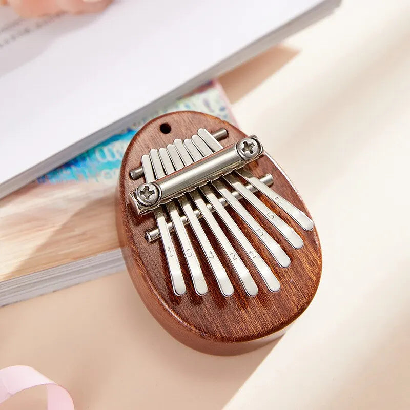 A compact oval wooden thumb piano musical toy with 8 silver metal tines marked for tones portable beginner use