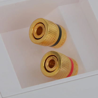 Gold-colored binding post banana plug audio connectors with knurled surfaces and black red bands in white box for audio surround wall