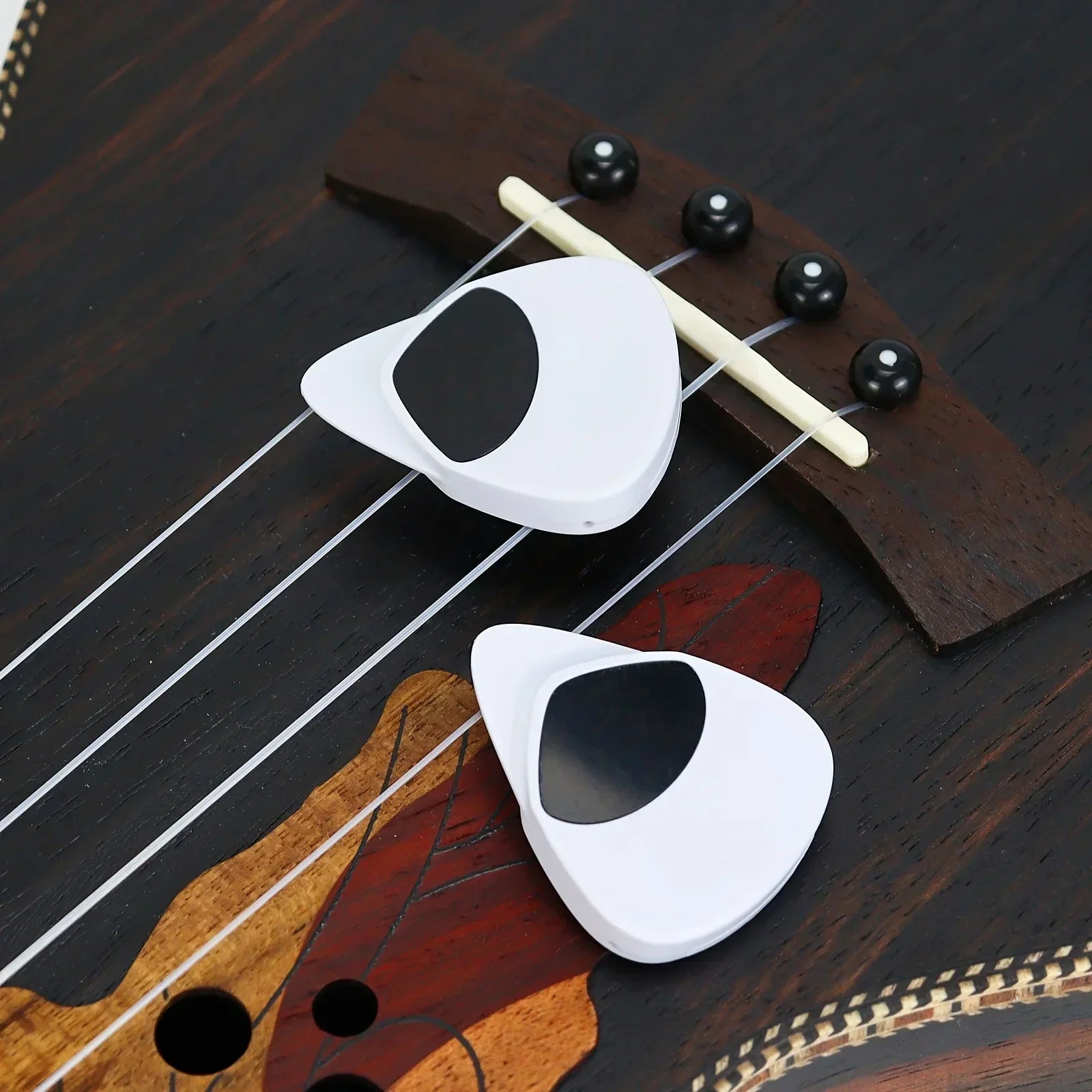 White plastic 2-in-1 guitar pick with black oval cutouts and multi-purpose pitch calibrator on dark wooden instrument