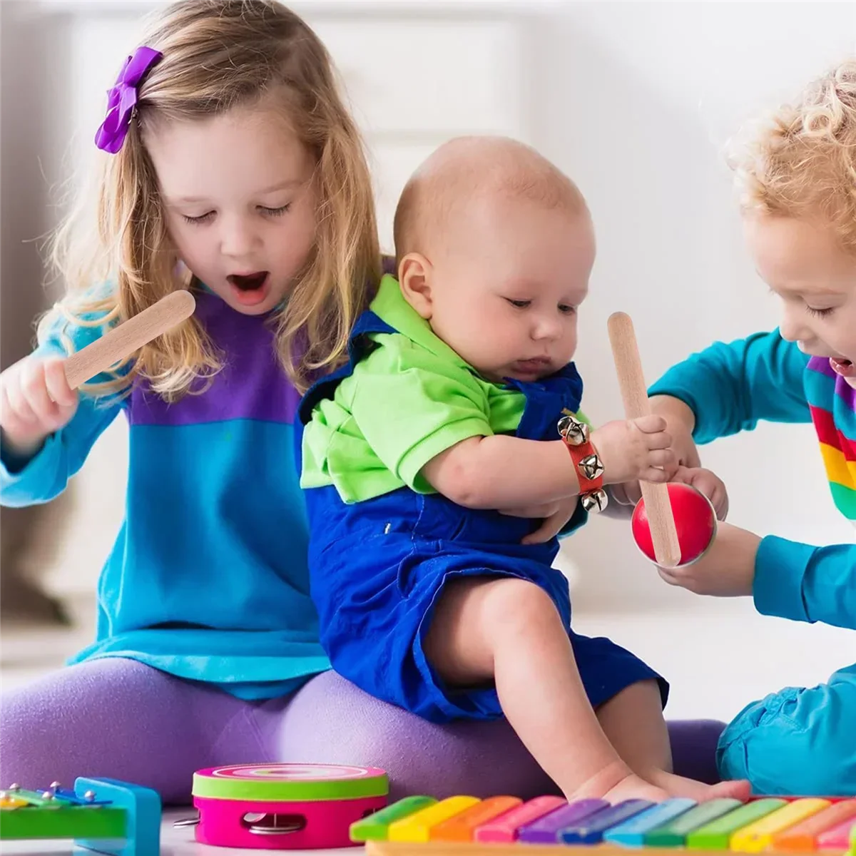 A baby wearing blue overalls holds a red tambourine alongside 8 inch kids rhythm sticks lummi sticks classical wood claves
