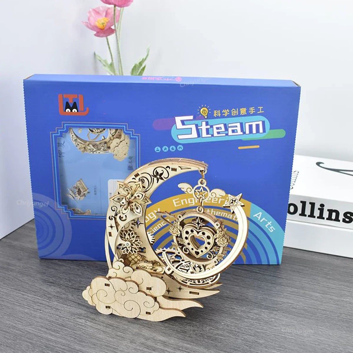 Intricately designed golden wooden puzzle moon 3d model with floral and gear details in front of blue packaging box