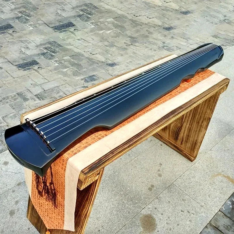 A sleek glossy black guqin zither handmade with seven strings on a wooden stand with accessories chinese traditional