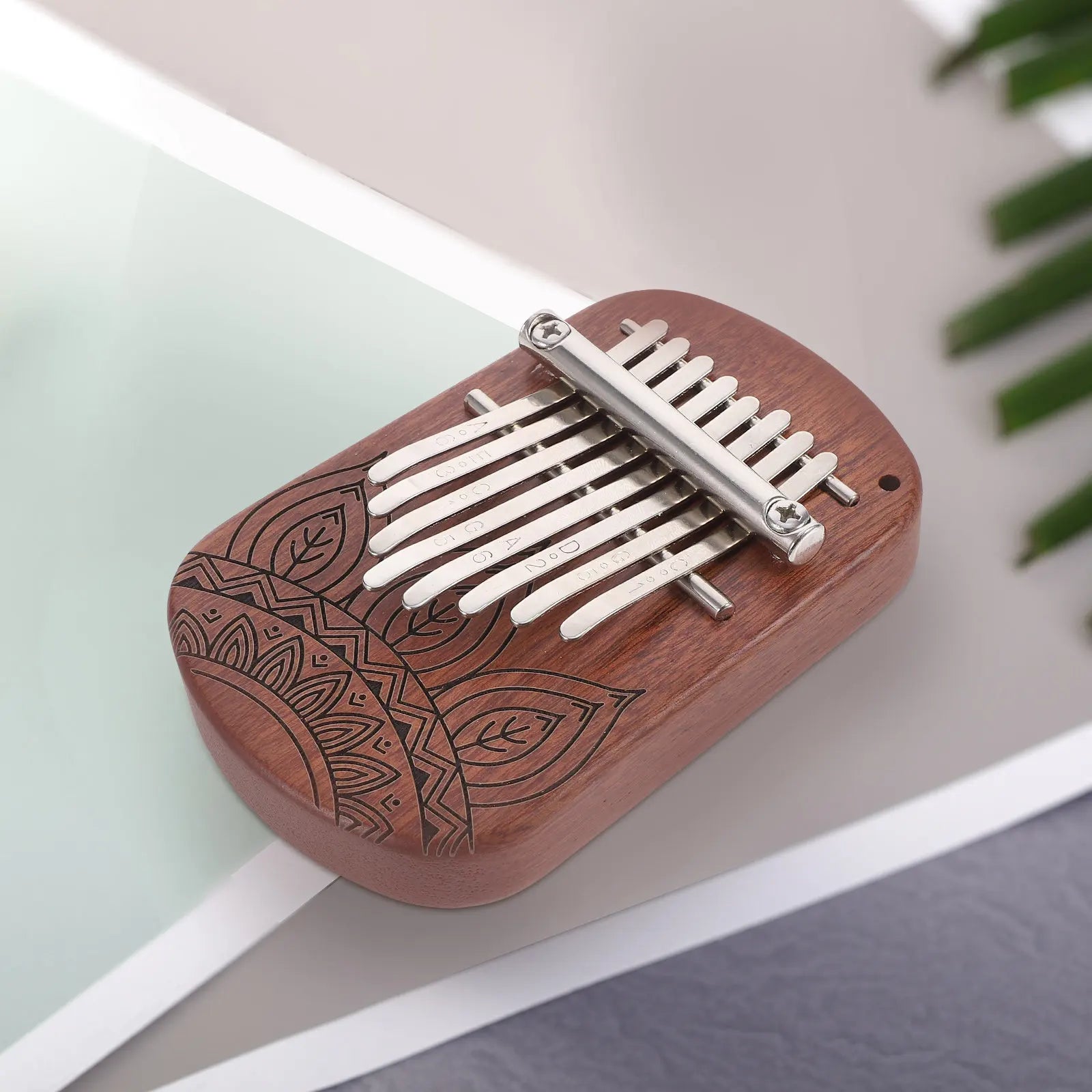 A wooden mini kalimba thumb piano with ten silver tines and leaf engraving for beginners kids adults portable use
