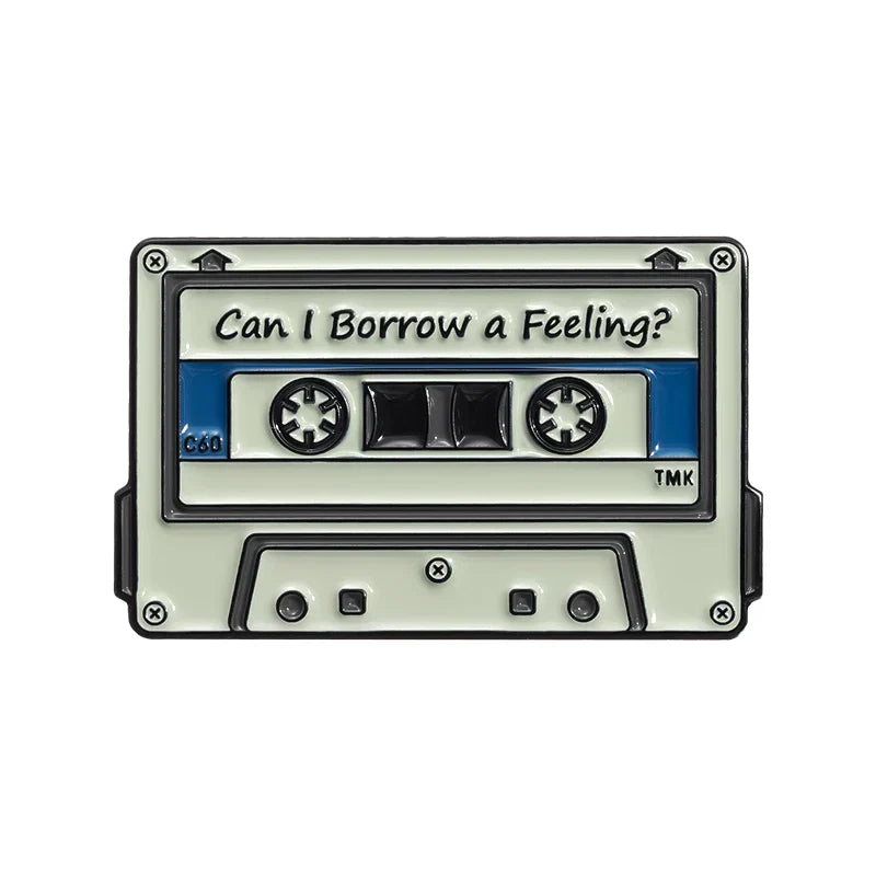 Vintage enamel pin of a cream cassette tape with blue label and text can i borrow a feeling from 90s retro music collection
