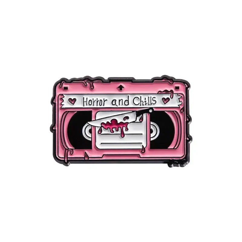 Pink enamel pin shaped like a cassette tape with horror and chills text and knife design from 90s retro music cassette tape collection