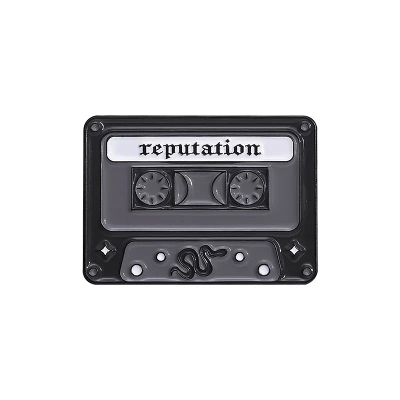 Black enamel pin shaped like a cassette tape with reputation label and snake design from 90s retro music collection