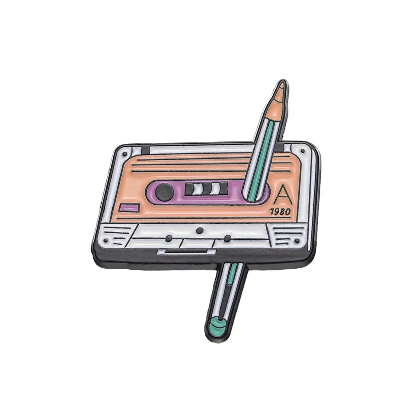 Pastel peach and lavender enamel pin shaped like a cassette tape with a green pencil for 90s retro music collection