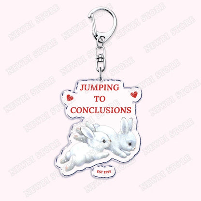 White acrylic keychain featuring two rabbits and jumping to conclusions text with silver clasp for aesthetic coquette pink womens accessories ribbon hot girl book gifts