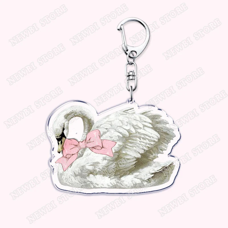 A clear acrylic aesthetic coquette pink keychain with a white swan, gray feathers, and womens accessories ribbon