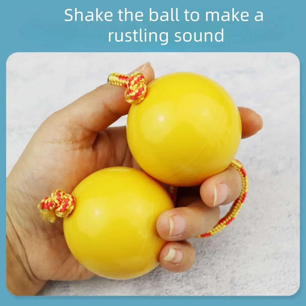 Two bright yellow african shaker kashaka rhythmic balls with red and gold braided cords tied to smooth tops