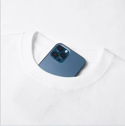A sleek deep blue iphone 12 pro with triple-lens camera nestled in the neckline of a white cotton short sleeve t-shirt
