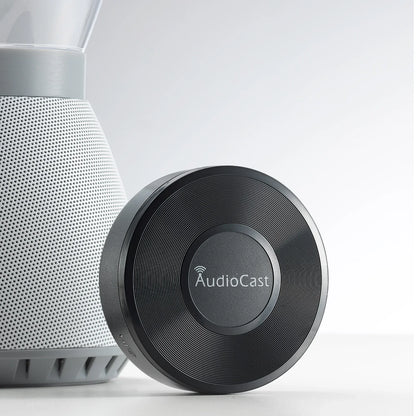 Black circular audiocast m5 music audio streamer with textured ribbed surface and silver logo for airplay audio music use