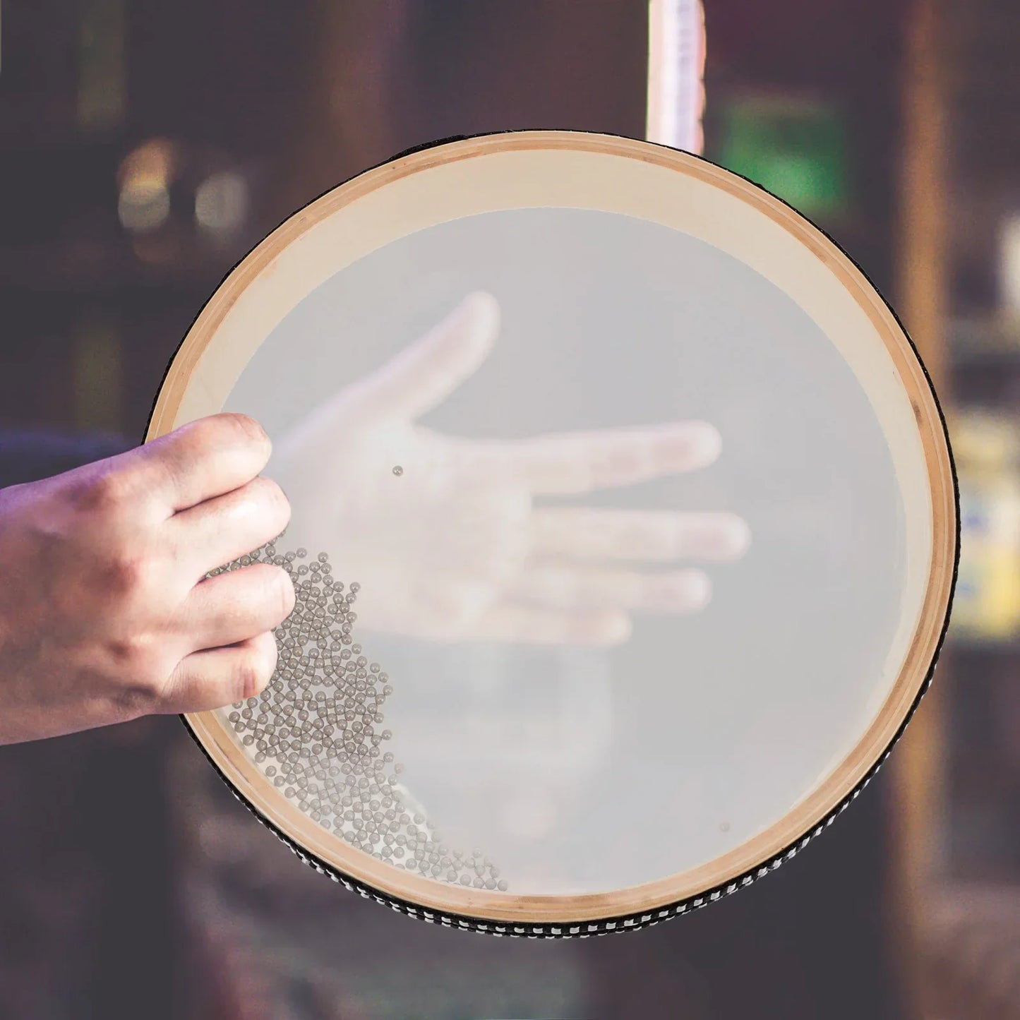 A hand gently holds a light wood framed baby montessori ocean bead hand drum toy for early learning music