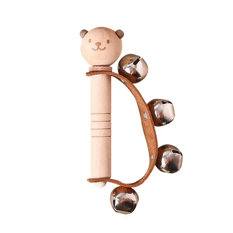 A light wood bear-shaped baby montessori toy rattle with four metallic bells on a brown leather strap for early sensory educational use