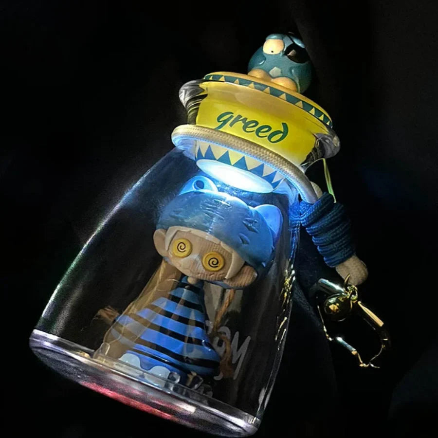 A blue and black striped bottle music blind toy with spiral eyes inside a glass bottle and a yellow lid labeled greed