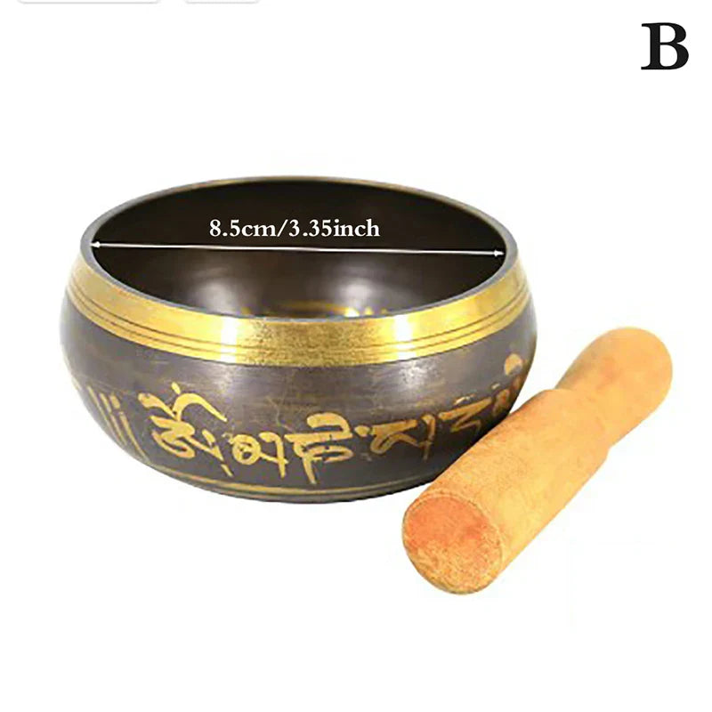 A dark bronze metal singing bowl with a gold rim and engraved sanskrit script alongside a wooden mallet for bell yoga meditation