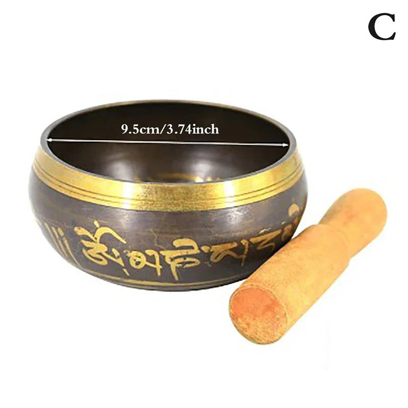 Dark bronze metal singing bowl with gold trim and engraved sanskrit script with wooden mallet for bell yoga meditation