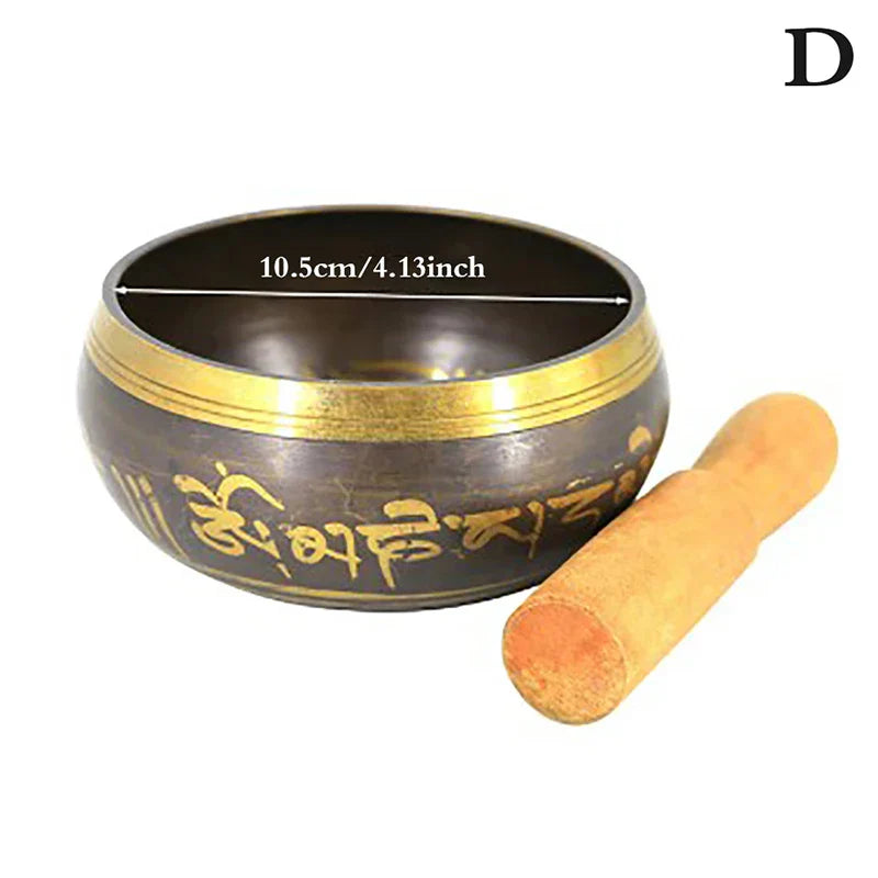 A dark bronze metal singing bowl with gold trim and engraved sanskrit script with wooden mallet for bell yoga meditation