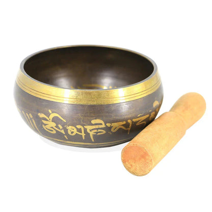 A dark bronze metal singing bowl with gold sanskrit inscriptions and a wooden mallet for bell yoga meditation use