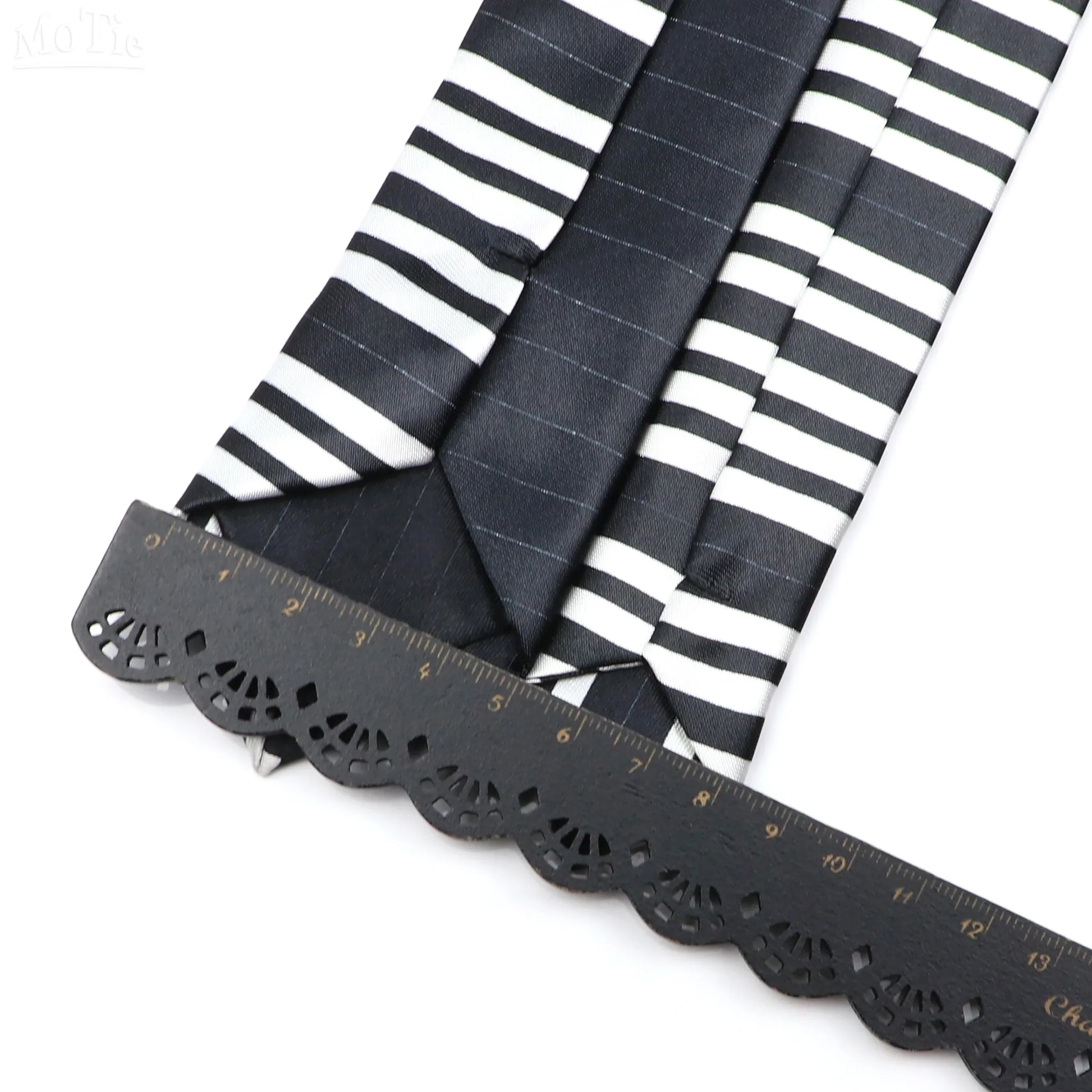 Black and white silky narrow neckties with classic musical notes and subtle pinstripe pattern displayed with black ruler