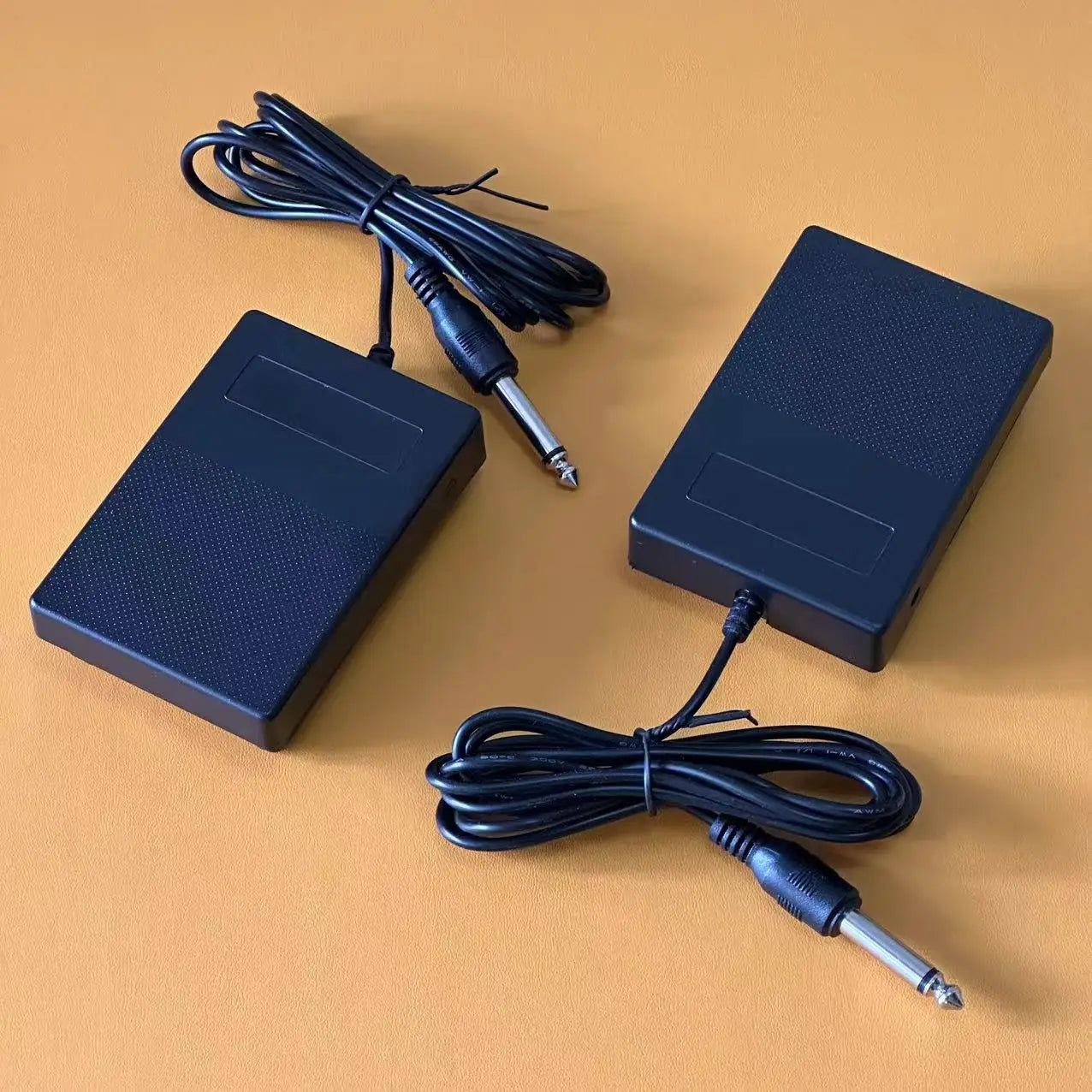 Black plastic compact sustain pedal with textured surfaces and silver-tipped cables for keyboards and drum machines