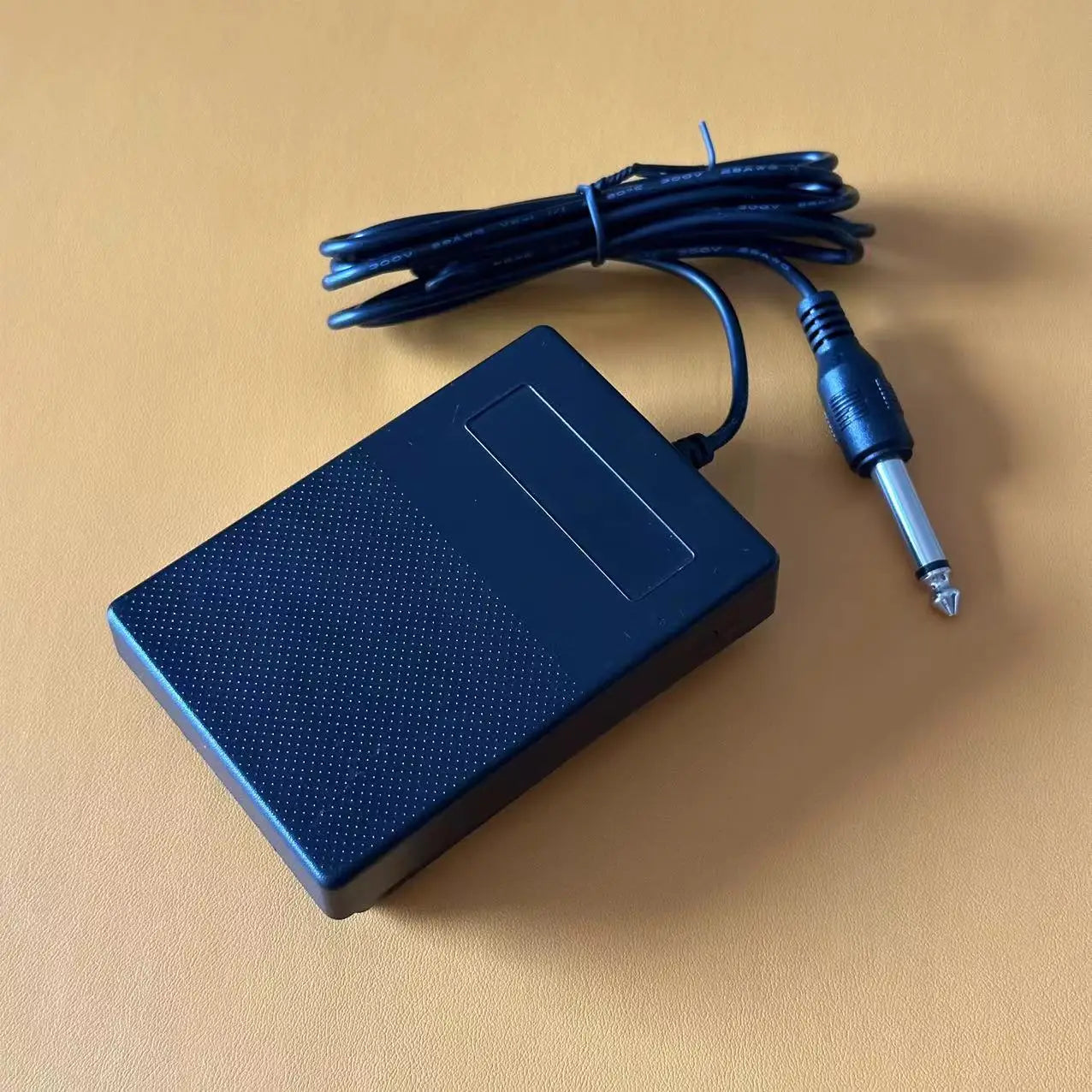 Black plastic compact sustain pedal with textured surface and coiled cable for keyboards drum machines and synthesizers