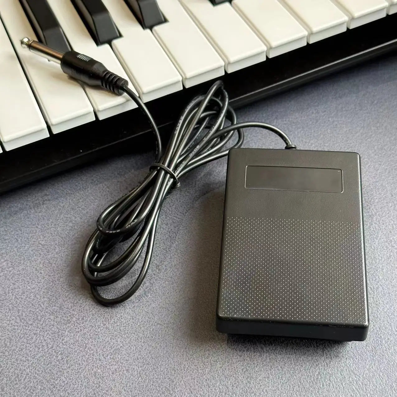 Black plastic compact sustain pedal with textured surface and coiled cable for keyboards and drum machines