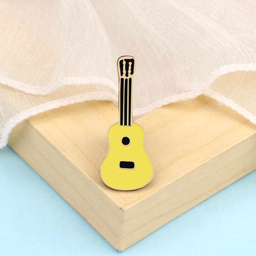 A bright yellow enamel fashion guitar microphone brooch with black details on a wooden surface for musician gifts