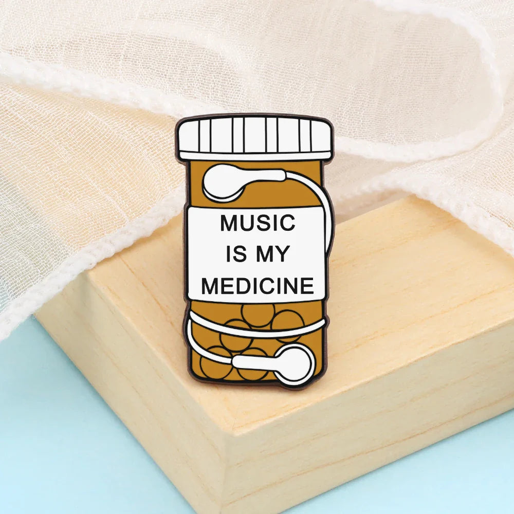 A charming enamel pin shaped like an orange prescription pill bottle with music is my medicine label and white earbuds ideal for music note enamel and piano notes lapel collections