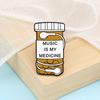 A charming enamel pin shaped like an orange prescription pill bottle with music is my medicine label and white earbuds ideal for music note enamel and piano notes lapel collections