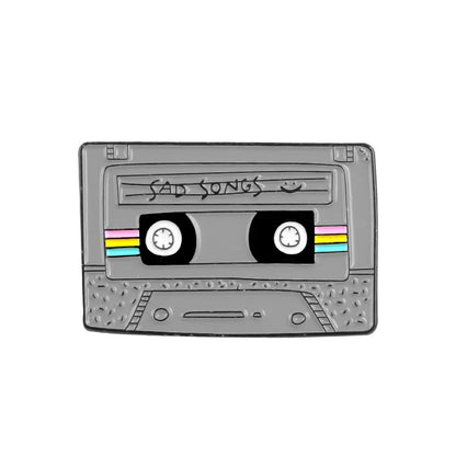 Gray enamel pin shaped like a cassette tape with sad songs label and rainbow stripes in headset alloy brooch style
