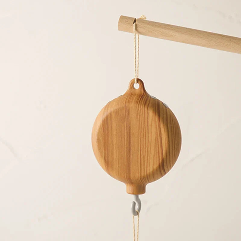 A light brown wooden crib bell rotary with natural wood grain and metal hook to enhance hand-eye coordination